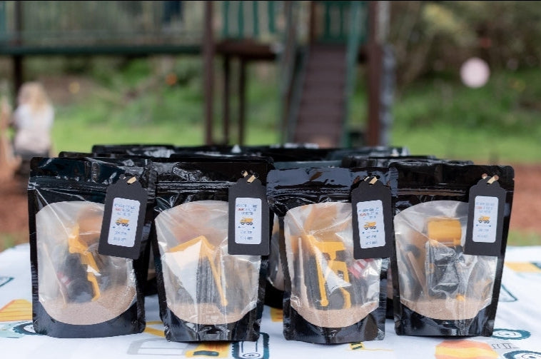 Party bags with personalised thank you label. Bags have a clear window showing the contents of diggers and sand. They are displayed nicely on a consturction party table cloth and park behind