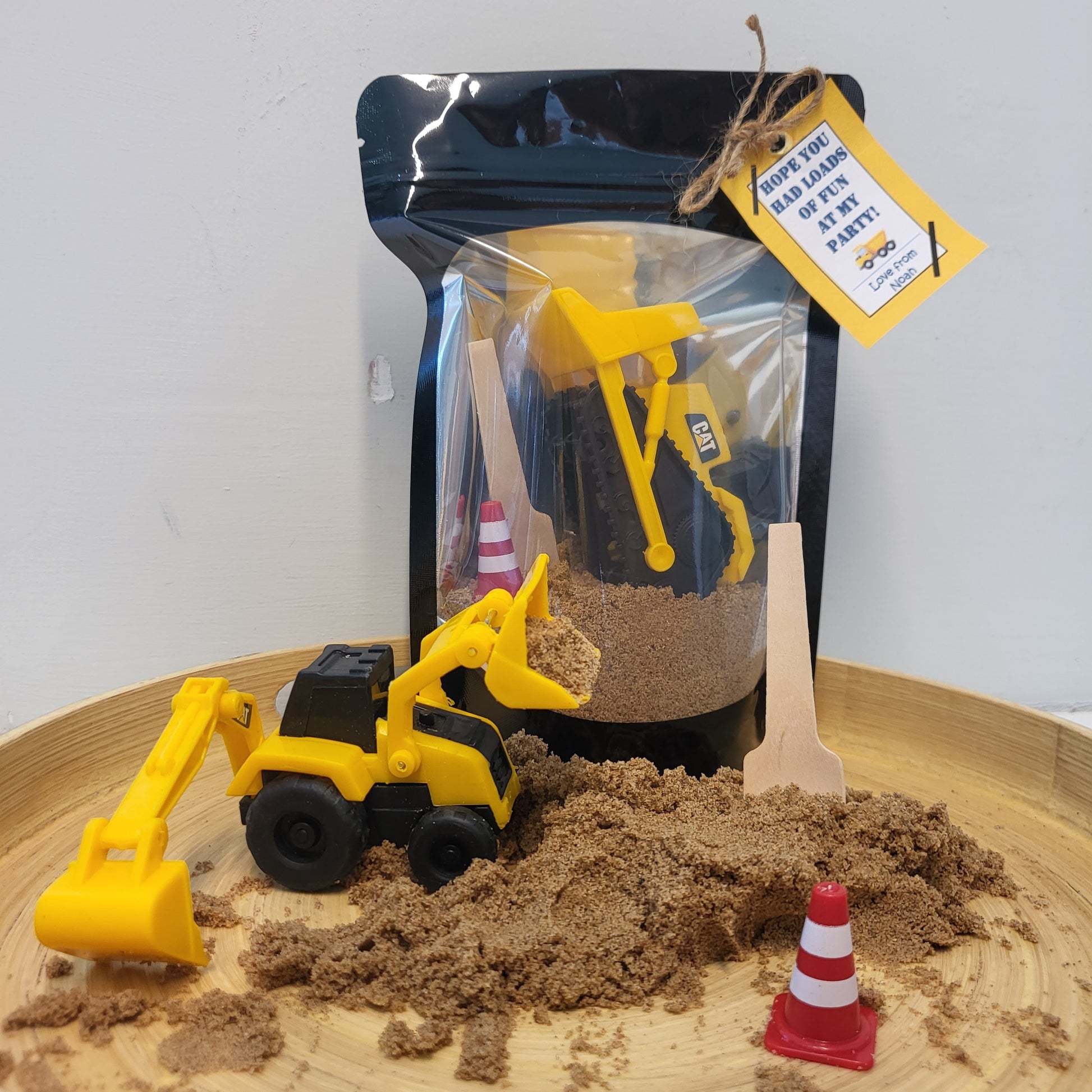 Clear front sealable party bag filled with sand, toy construction vehicle, play cone and wooden mini spade