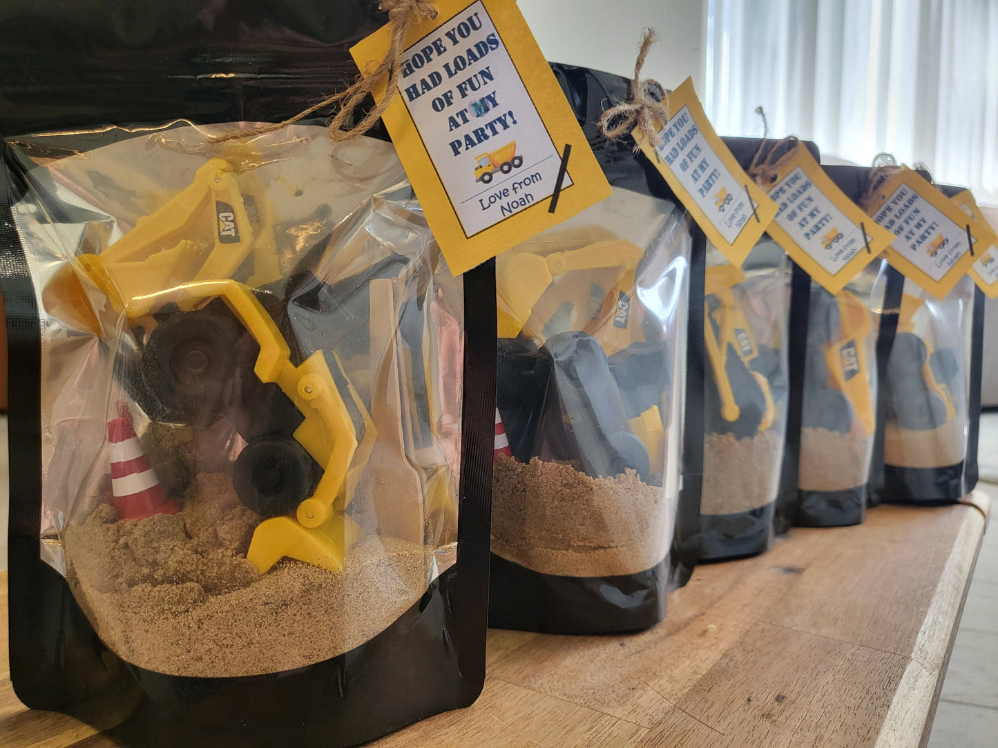 Clear Sealable childrens party bag filled wil digger, sand, cone and space with personalised tag, saying 'hope you had loads of fun at y party, love from Noah'.  The party favours are lined up making a lovey dislay for a party